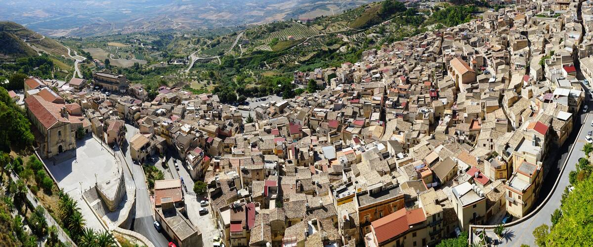 A densely packed town with narrow streets and historic buildings, surrounded by hills and vineyards.