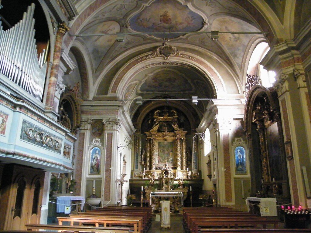 Interior ornamentado de una iglesia con un altar mayor, bancales y un órgano de tubos.