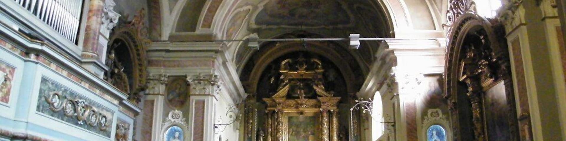 Interior ornamentado de una iglesia con un altar mayor, bancales y un órgano de tubos.