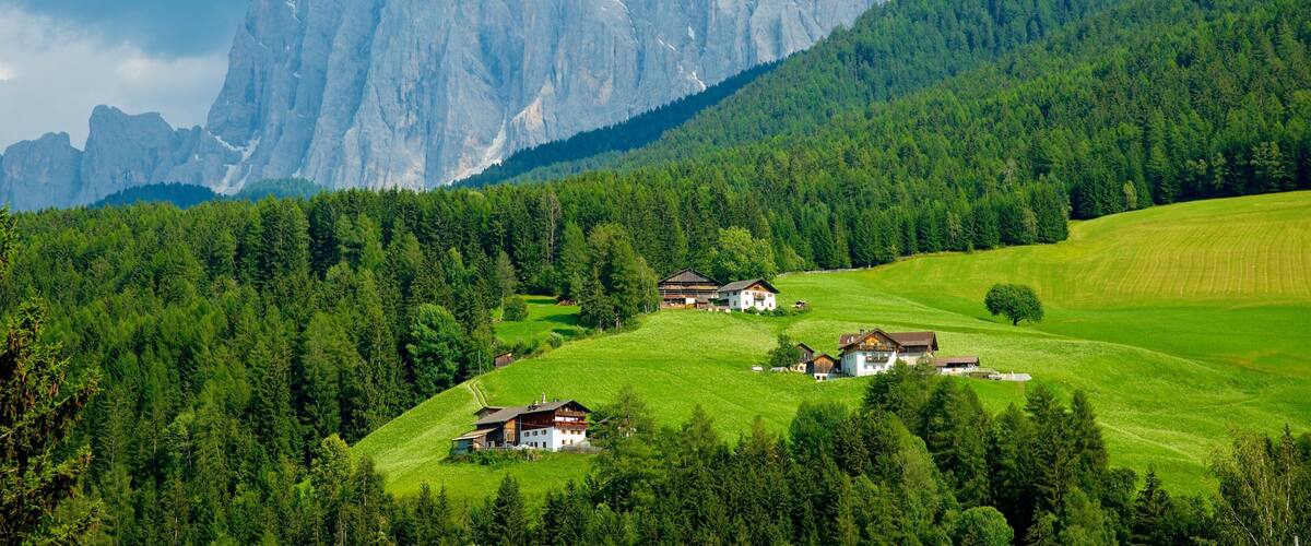 A mountainous landscape with a village nestled among lush green fields and dense forests.
