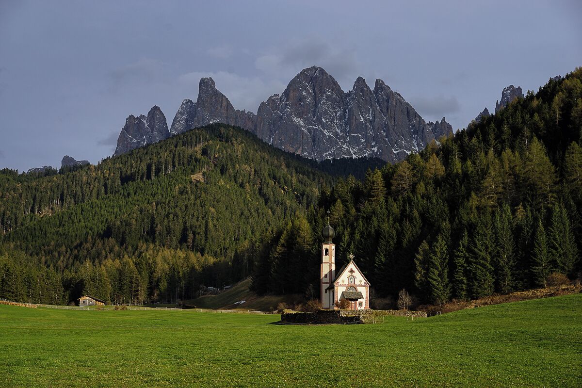 Una iglesia rodeada por un campo verde y una cadena montañosa boscosa.