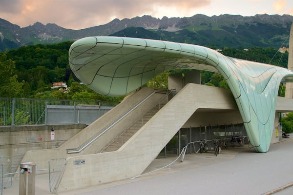 Ein modernes Bauwerk mit gewölbter Dachform und Treppe, die davor hinaufführt, vor einer Berglandschaft.