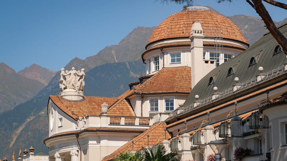 A historic building with a dome and statues, surrounded by mountains.