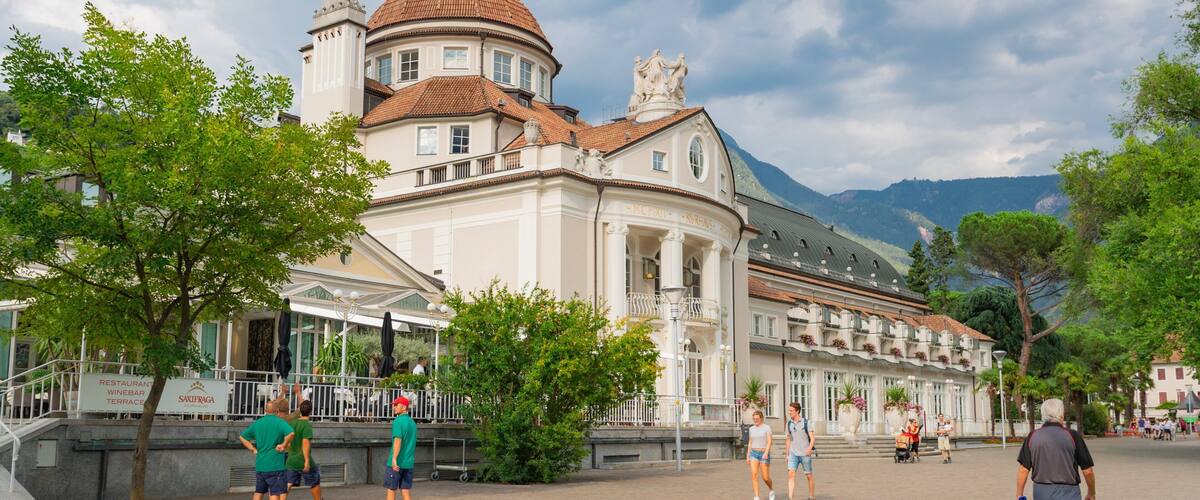 A historic building with a dome and classical architecture, surrounded by trees and a mountainous backdrop.