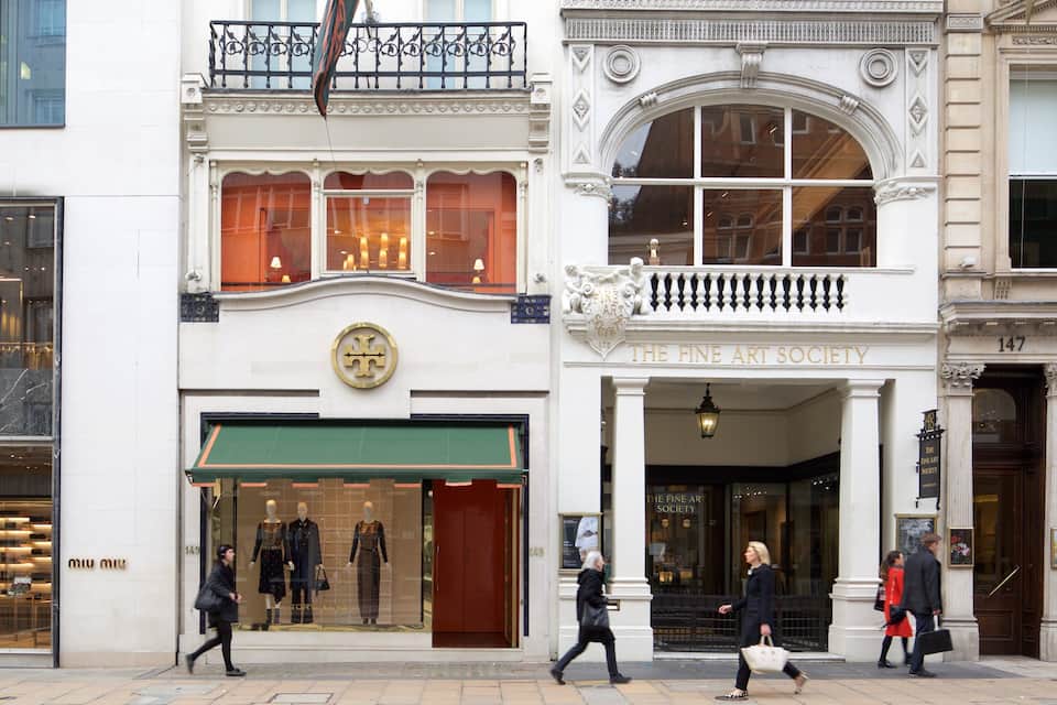 Una calle con una tienda llamada 'The Fine Art Society' y un edificio con un balcón.