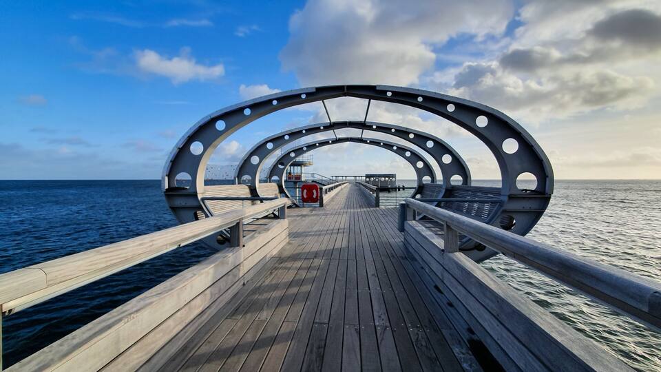 A wooden pier with circular metal railings extending into the sea.
