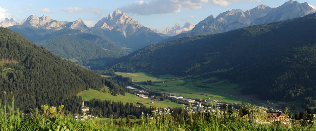 A valley with mountains in the background, a small town, and lush greenery.