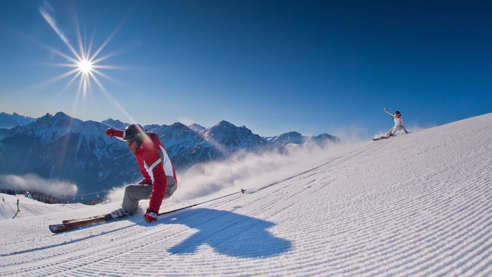 Ein Skifahrer in einer roten Jacke auf einem verschneiten Hang, im Hintergrund Berge.
