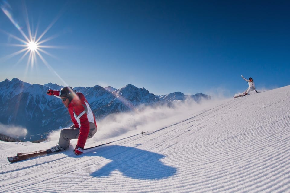 A skier in a red jacket on a snowy slope with mountains in the background.