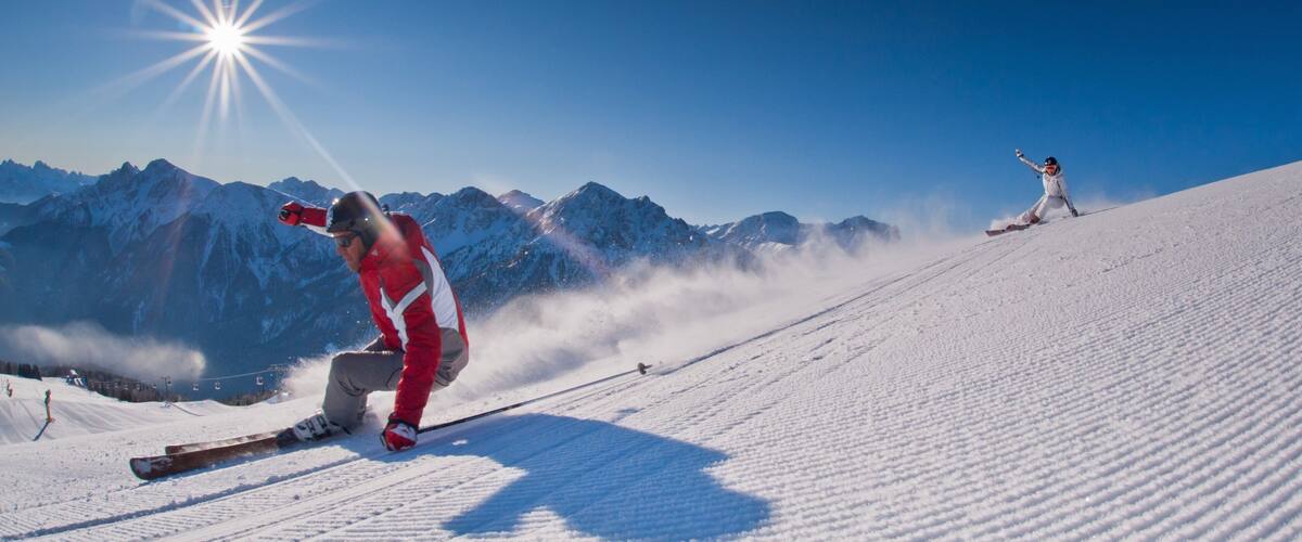 A skier in a red jacket on a snowy slope with mountains in the background.