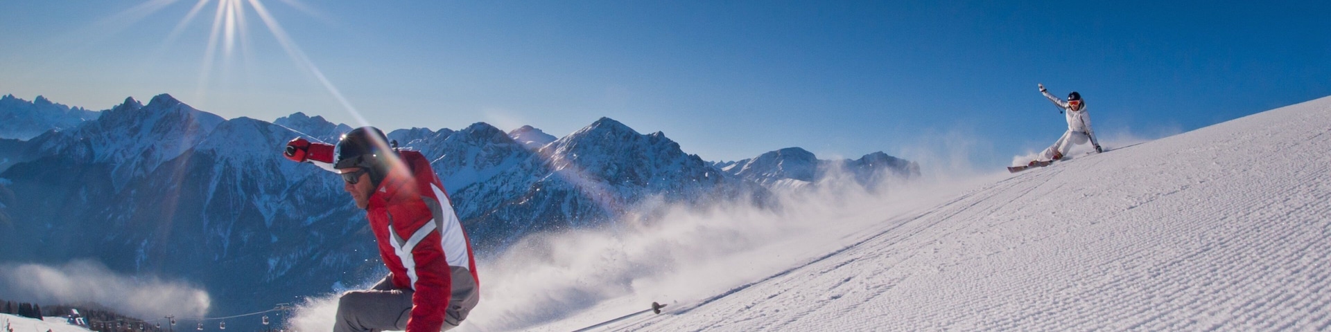 A skier in a red jacket on a snowy slope with mountains in the background.