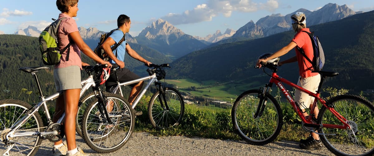 Three cyclists on a mountain path with a scenic view of mountains and a valley.