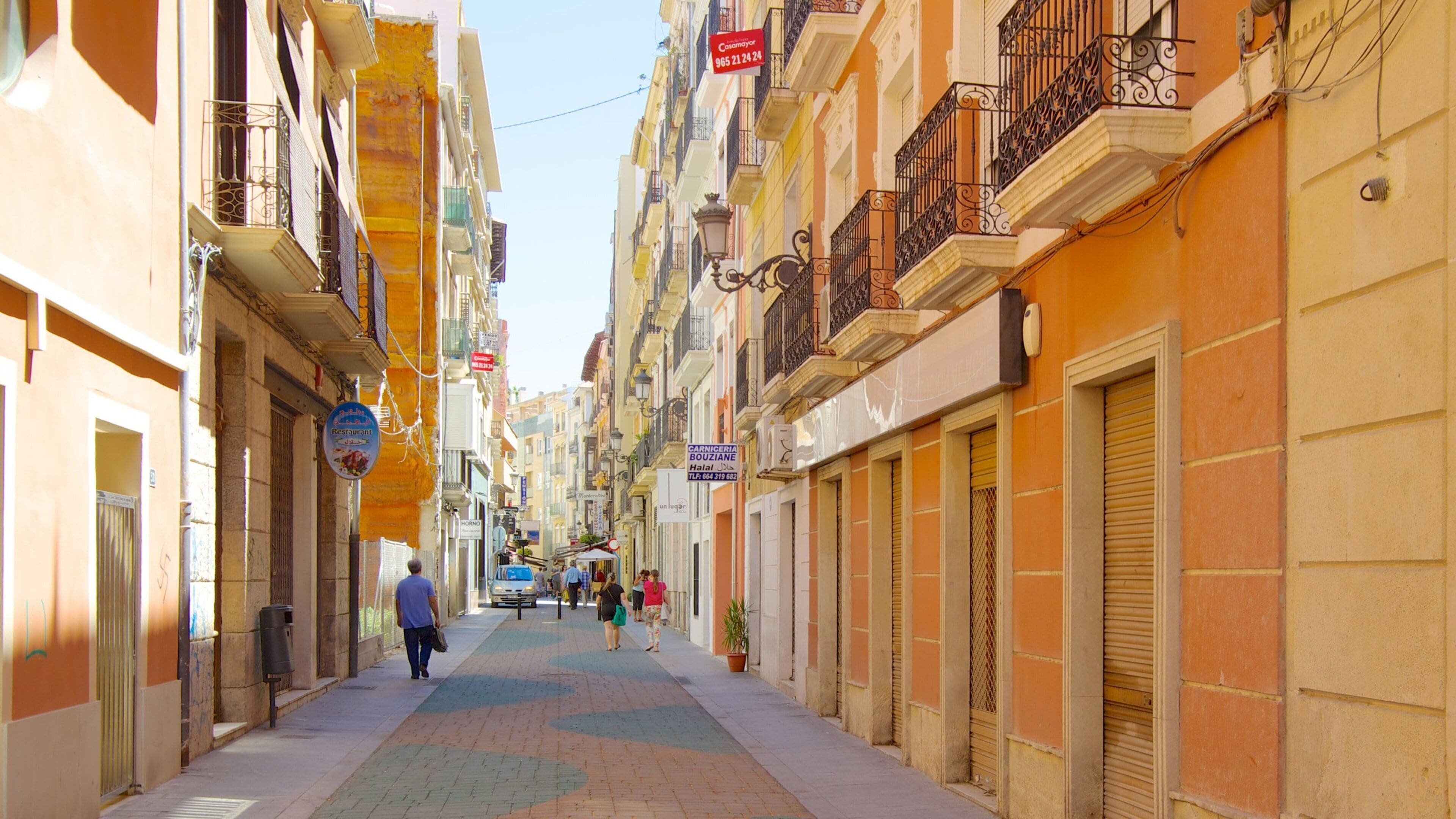 Una calle estrecha flanqueada por edificios de colores, un hombre caminando y un coche estacionado.