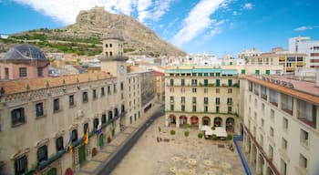 Una piazza con edifici storici, un’imponente torre dell'orologio e una collina con rovine sullo sfondo.