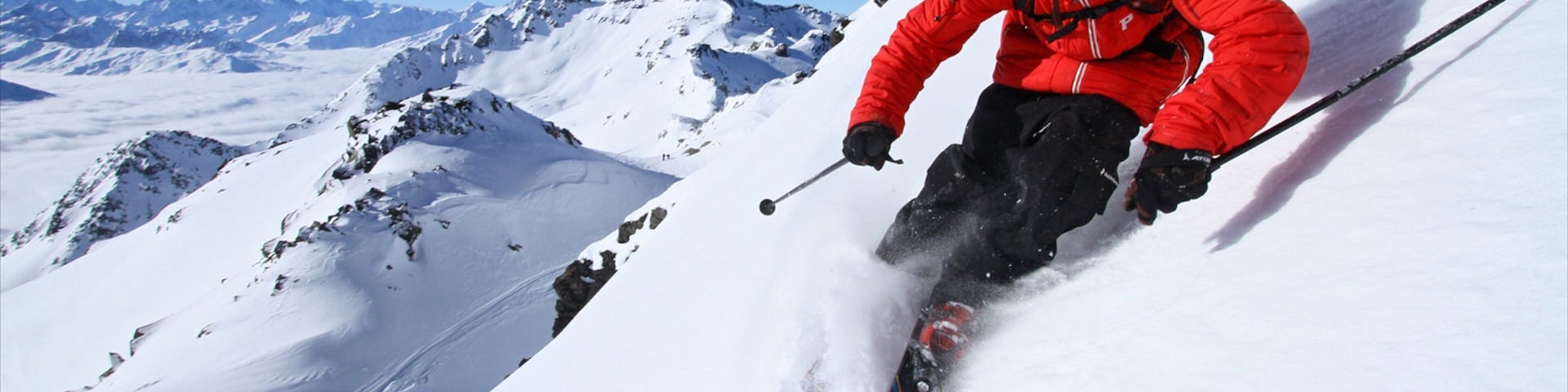 A skier in a red jacket skiing down a snowy mountain slope.
