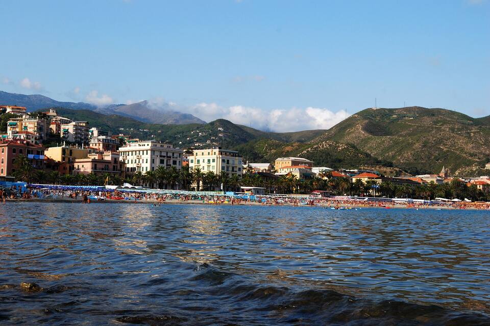 A coastal town with a beach, buildings, and mountains in the background.