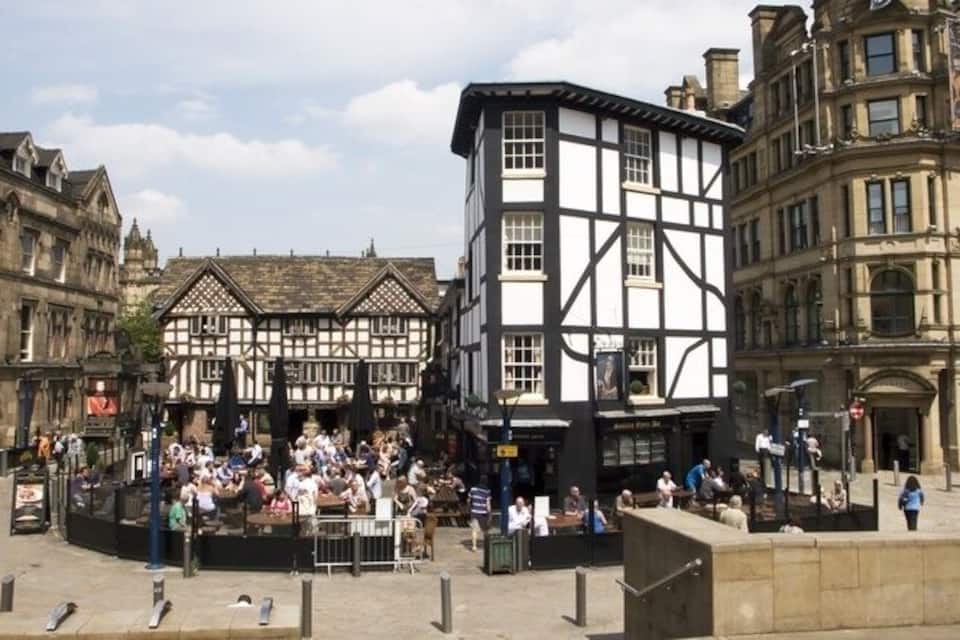 A bustling square with traditional half-timbered buildings, a central open space with people, and a prominent clock tower.