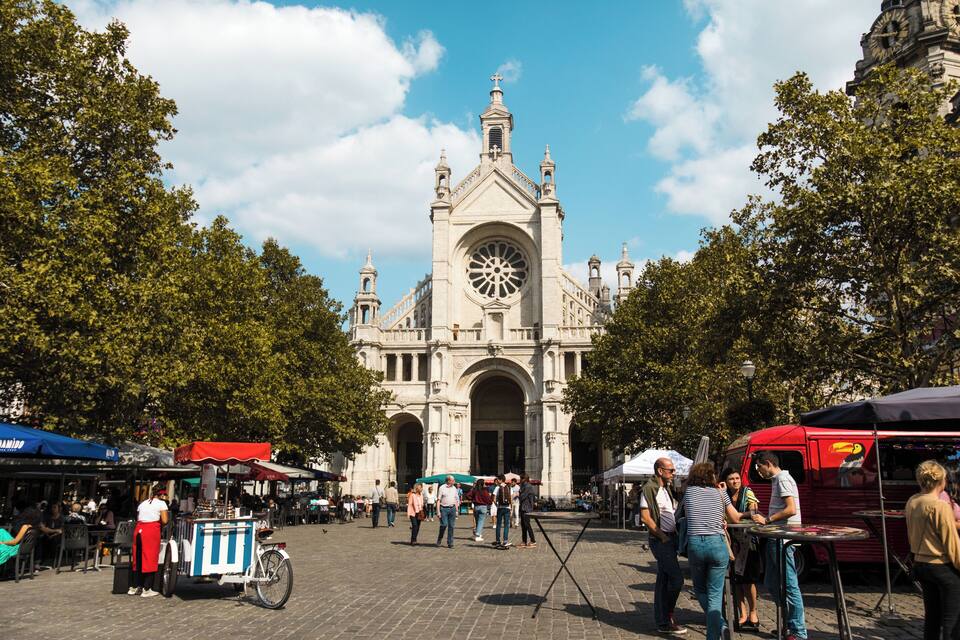 Een historisch kerkgebouw met een grote klokkentoren, omringd door bomen en mensen.