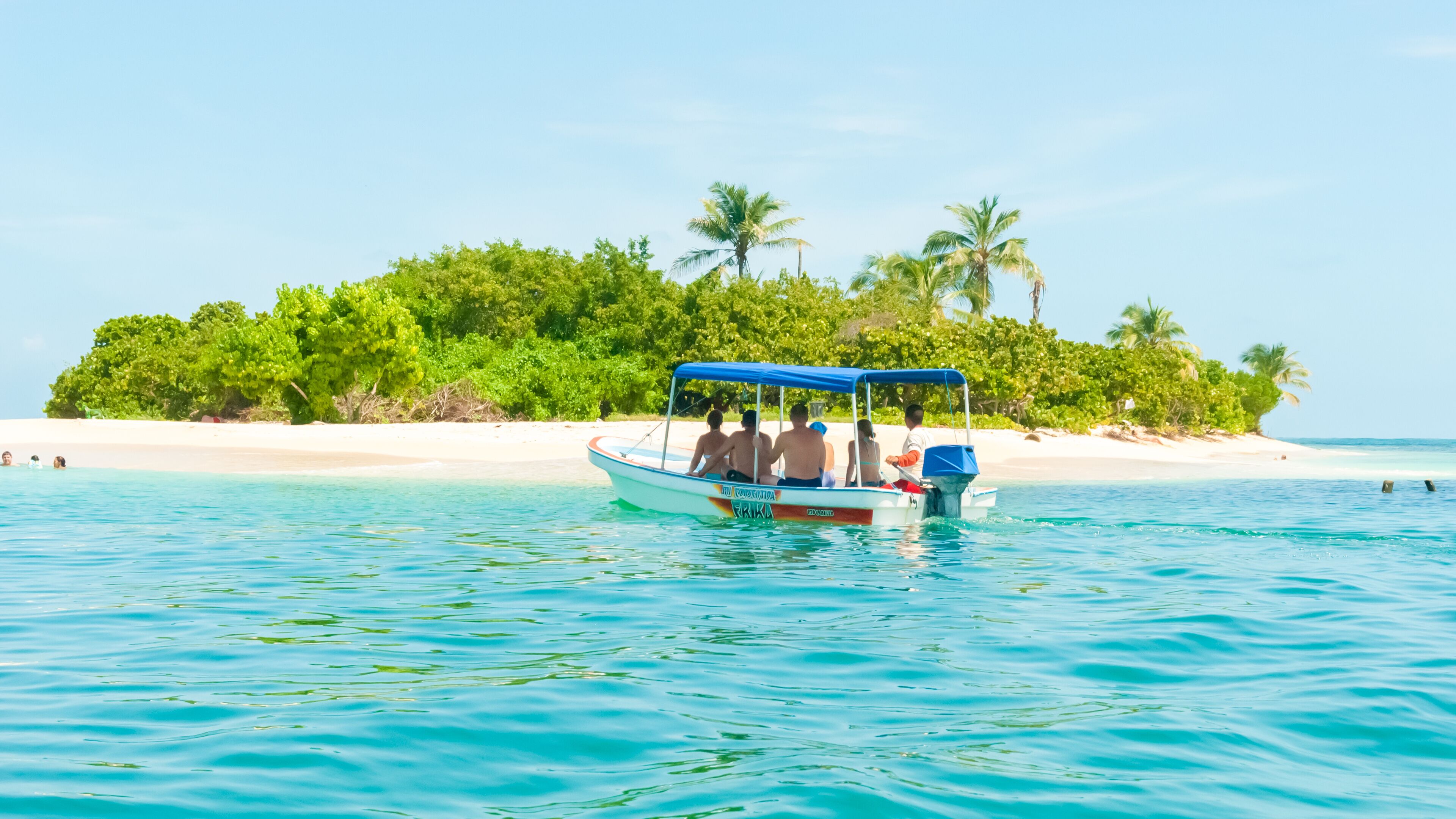 A boat on turquoise water with a beach and palm trees in the background.