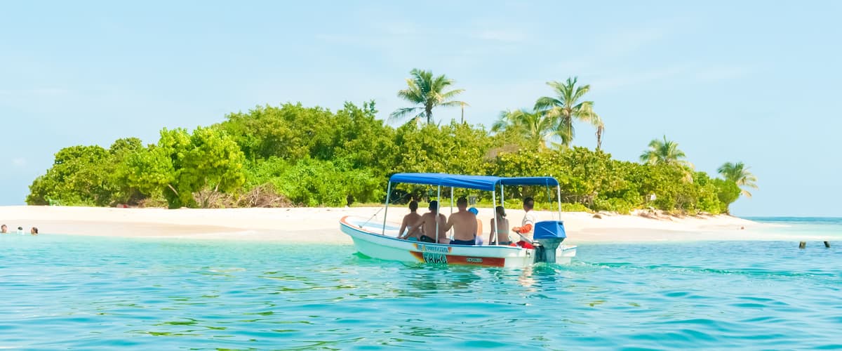 A boat on turquoise water with a beach and palm trees in the background.