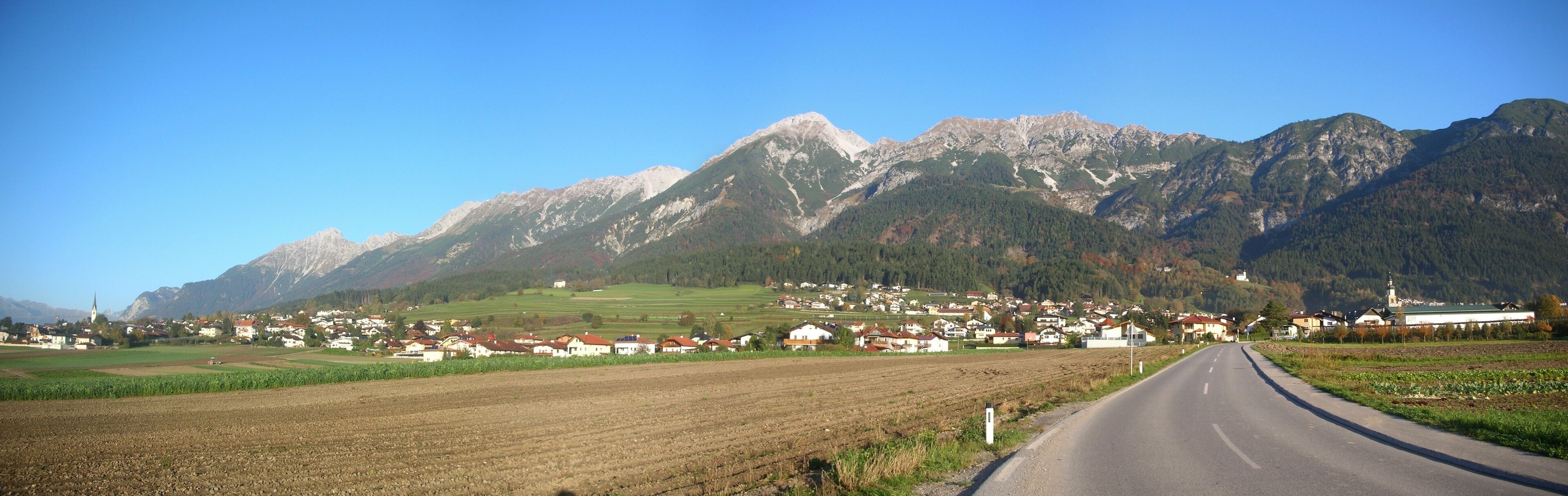 A rural road leading through a village with mountains in the background.