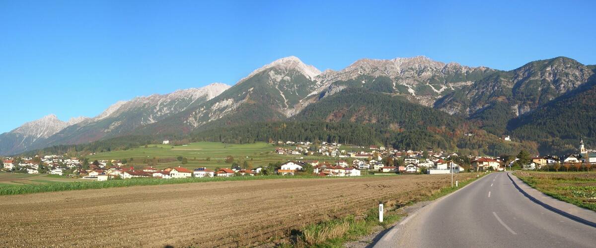 A rural road leading through a village with mountains in the background.