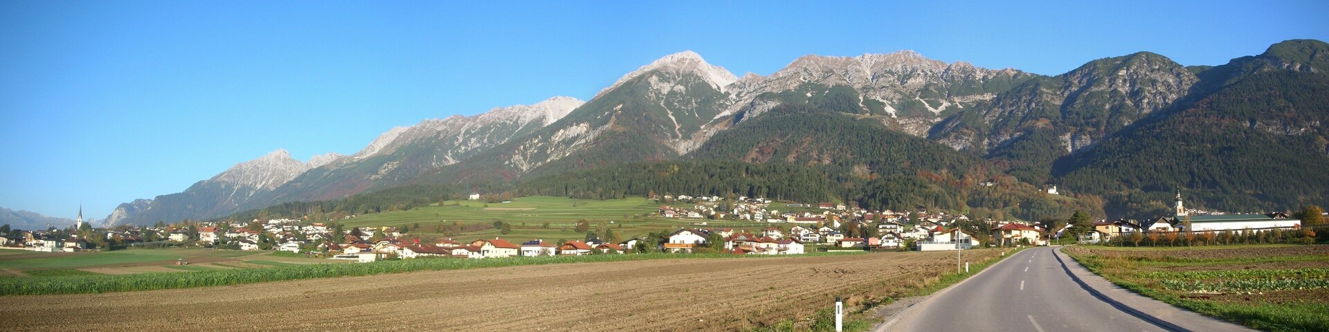A rural road leading through a village with mountains in the background.