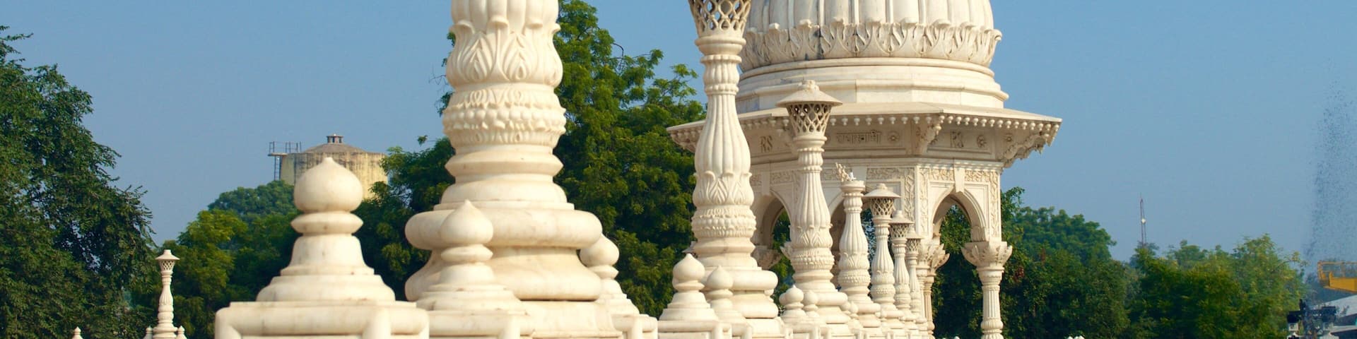 A white ornate pavilion with a dome and a tall pillar against a clear blue sky.