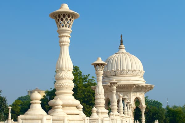A white ornate pavilion with a dome and a tall pillar against a clear blue sky.