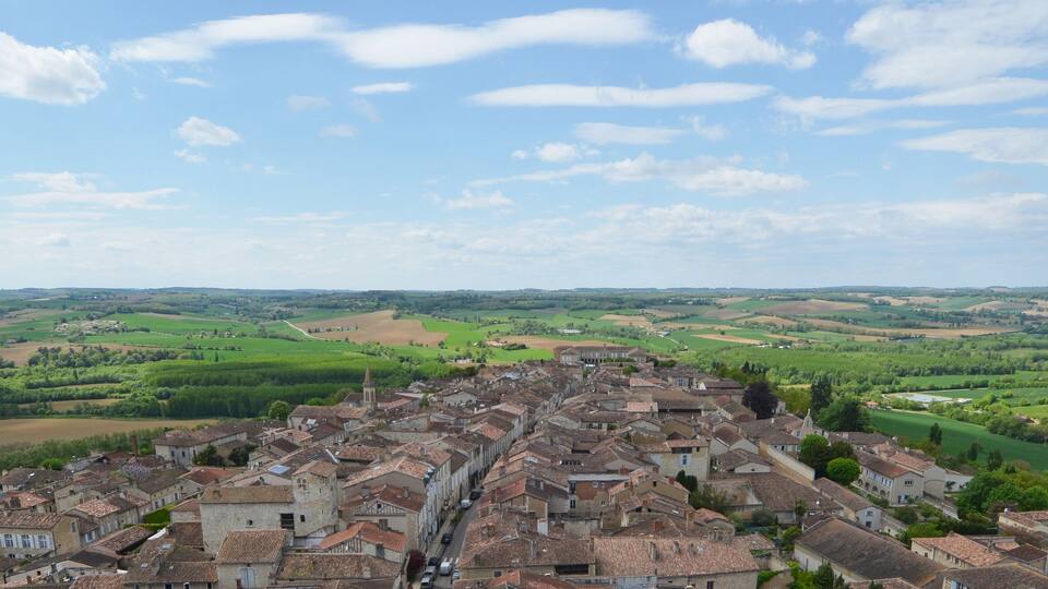 A historic town with terracotta-roofed buildings, surrounded by lush green fields and rolling hills.