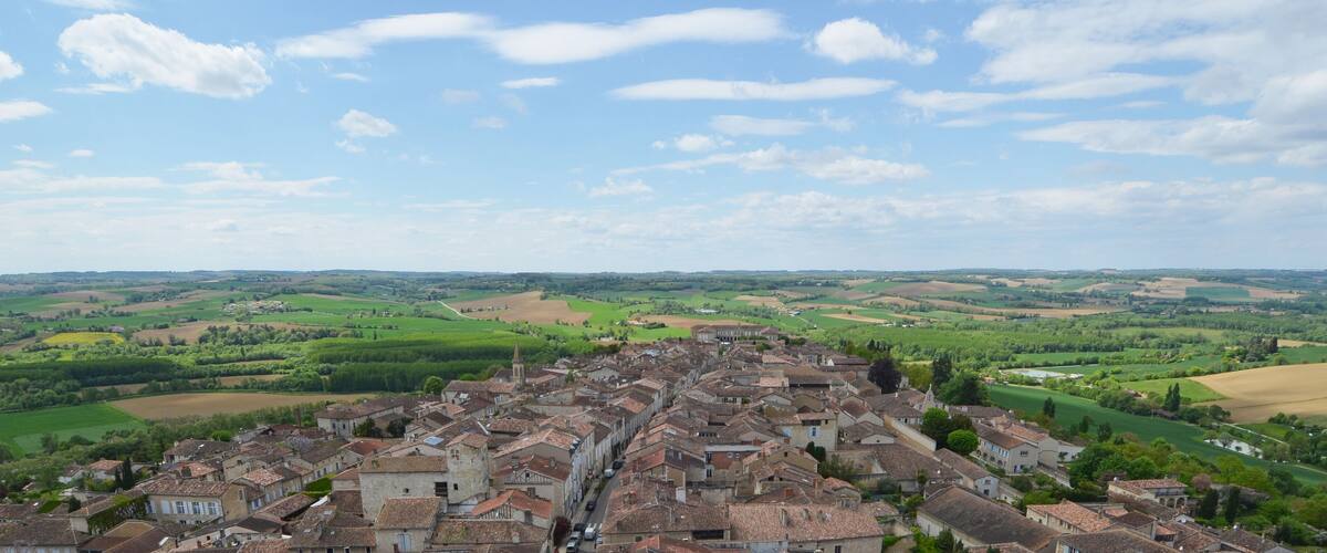 A historic town with terracotta-roofed buildings, surrounded by lush green fields and rolling hills.