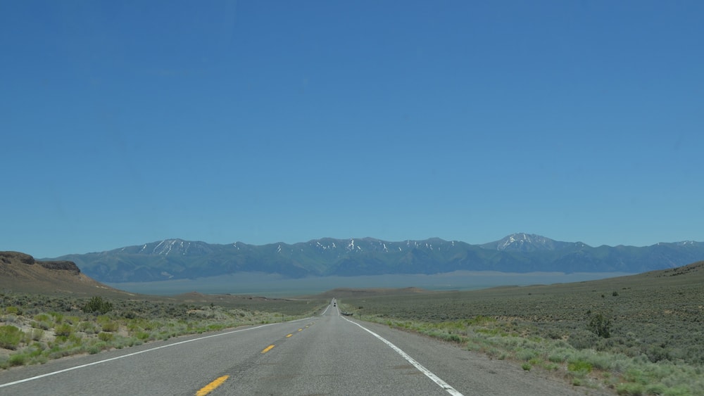 Une route qui mène à des montagnes aux sommets enneigés, sous un ciel bleu dégagé.
