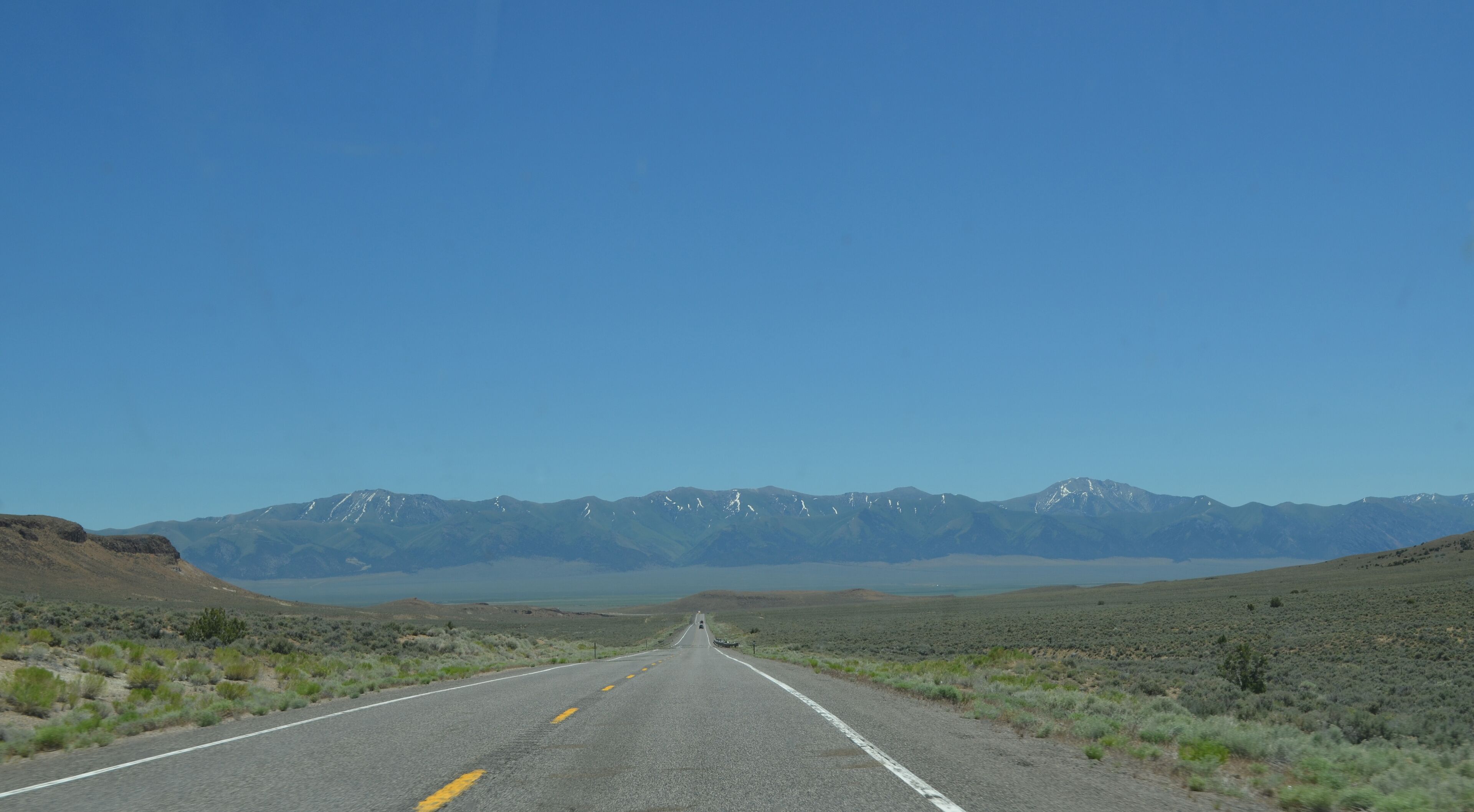 A road leading to snow-capped mountains under a clear blue sky.