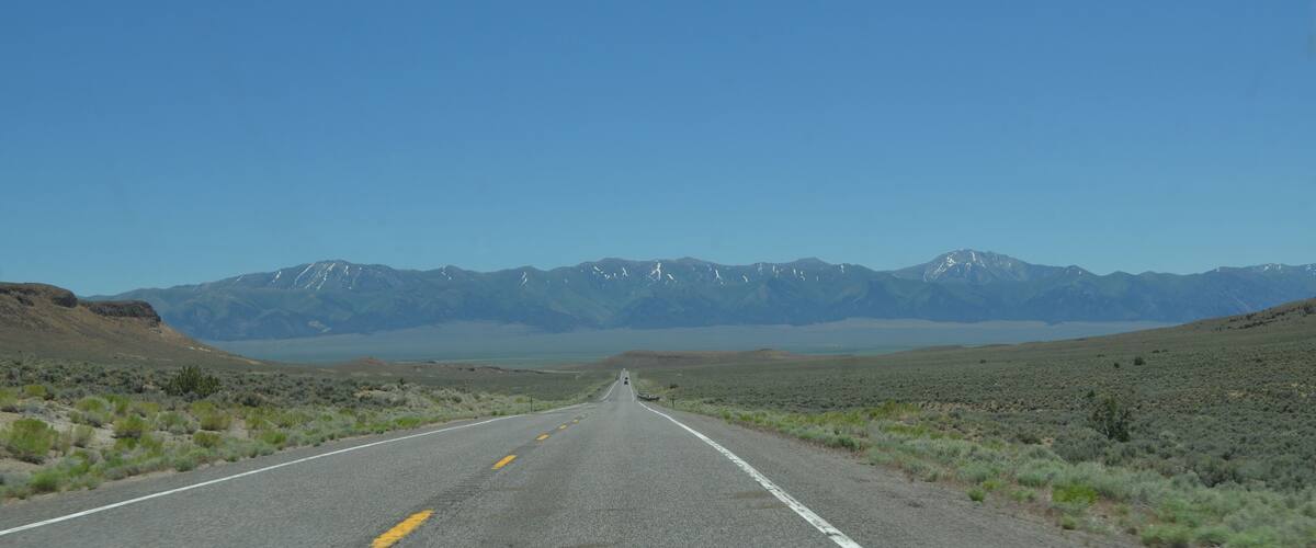 A road leading to snow-capped mountains under a clear blue sky.