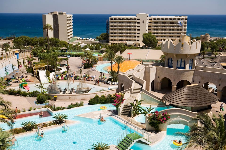 A resort with a large swimming pool, palm trees, and a castle-like structure.