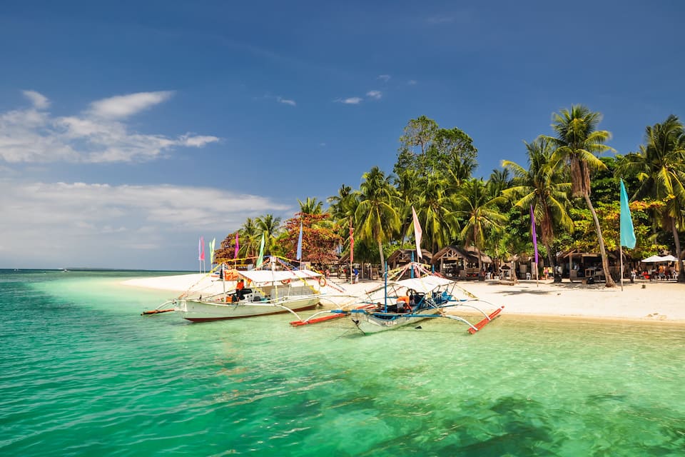 A beach with clear turquoise water, palm trees, and traditional boats.