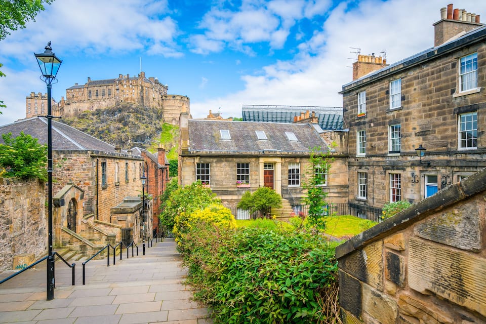 A stone pathway leading to historic buildings with a castle in the background.