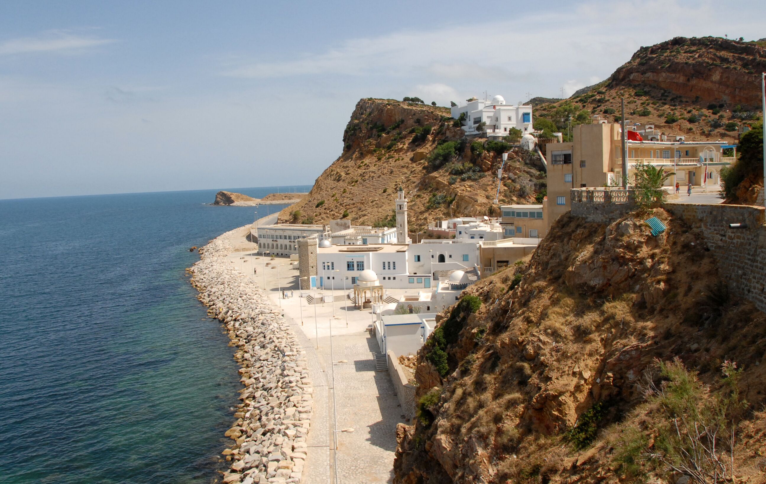 A coastal town with white buildings, a rocky shoreline, and a cliff overlooking the sea.
