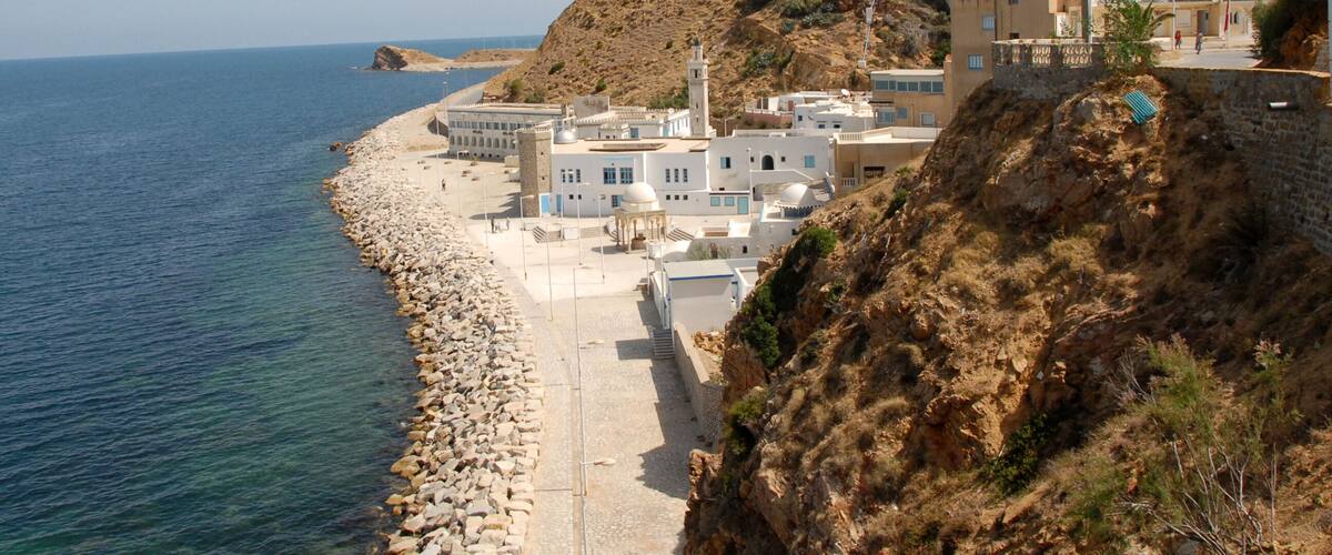 A coastal town with white buildings, a rocky shoreline, and a cliff overlooking the sea.