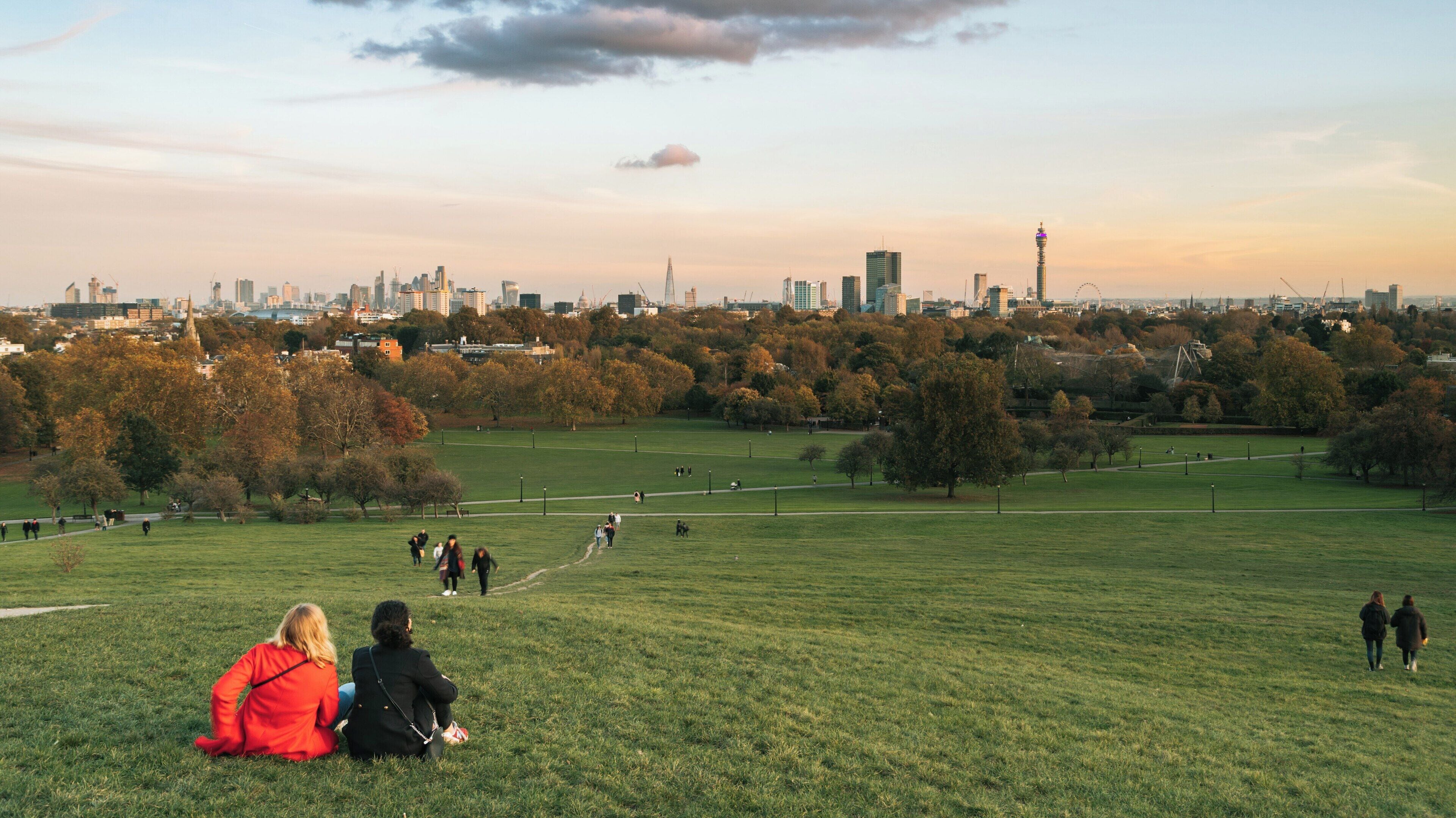 Visitors enjoy the view from Primrose Hill in Camden, London during a beautiful evening at sunset with a skyline view of the city