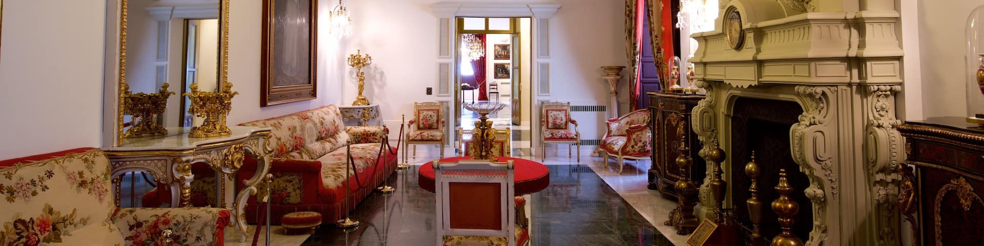 An opulent room with ornate furniture, a grand chandelier, and a classical fireplace.