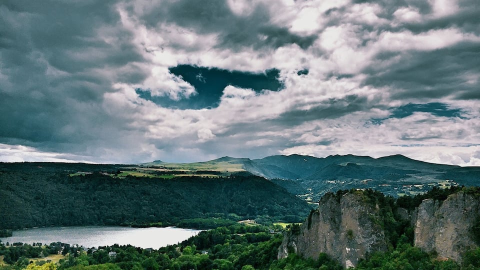 A mountainous landscape with a lake, dense forests, and rocky cliffs.