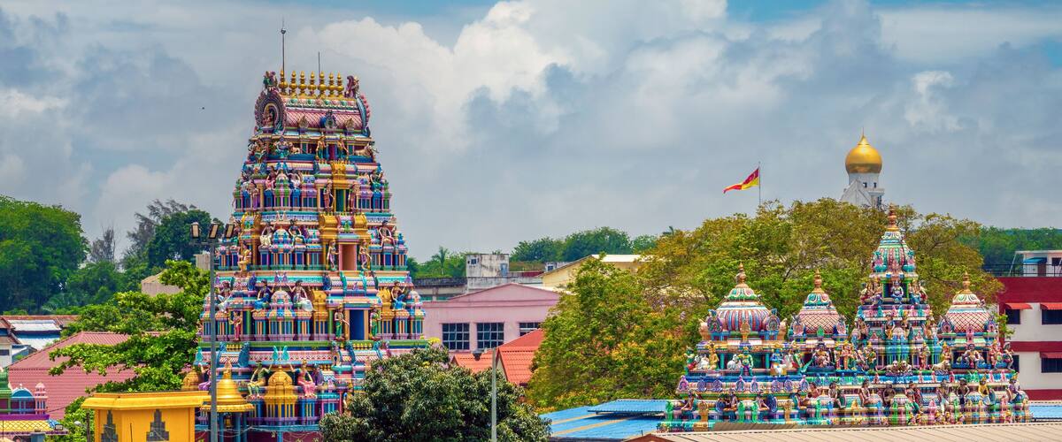 A colorful temple with intricate carvings and statues, surrounded by lush greenery and a clear blue sky.