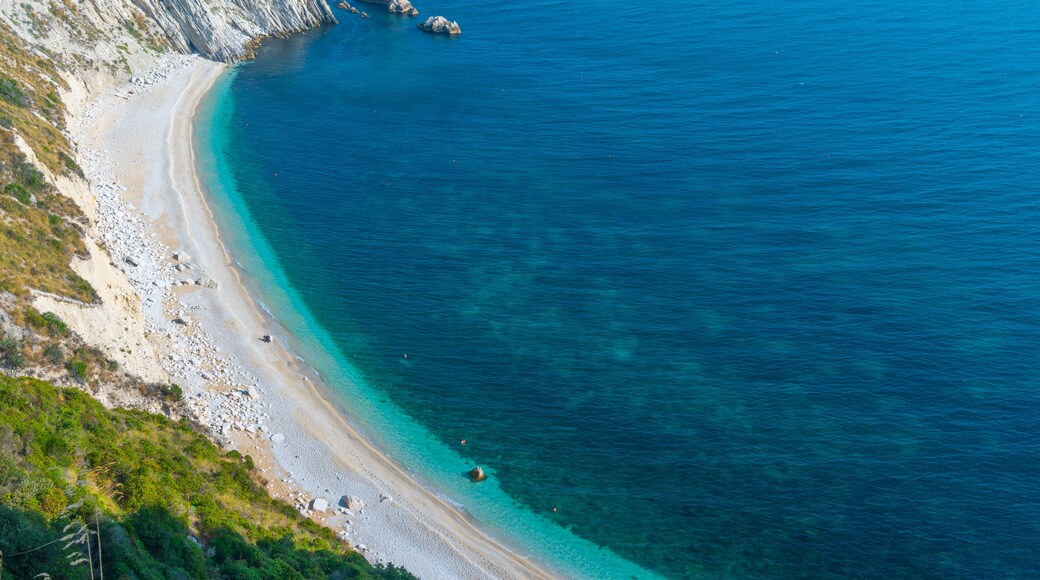 Un paysage cÎtier caractérisé par une plage de sable, des eaux turquoise et limpides, et des falaises rocheuses.