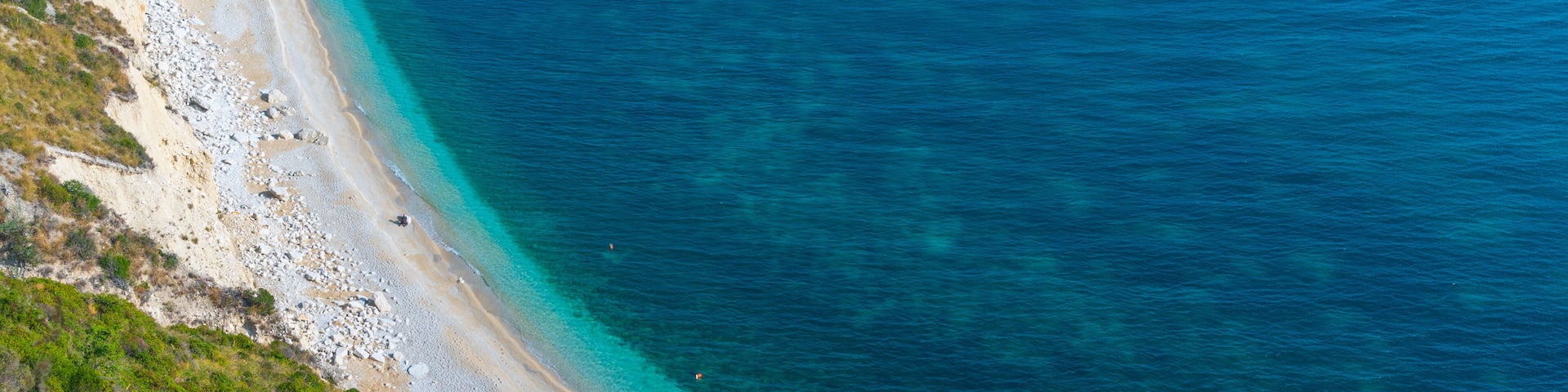 A coastal landscape with a sandy beach, clear turquoise waters, and rocky cliffs.