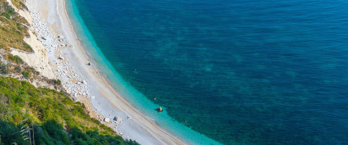 A coastal landscape with a sandy beach, clear turquoise waters, and rocky cliffs.