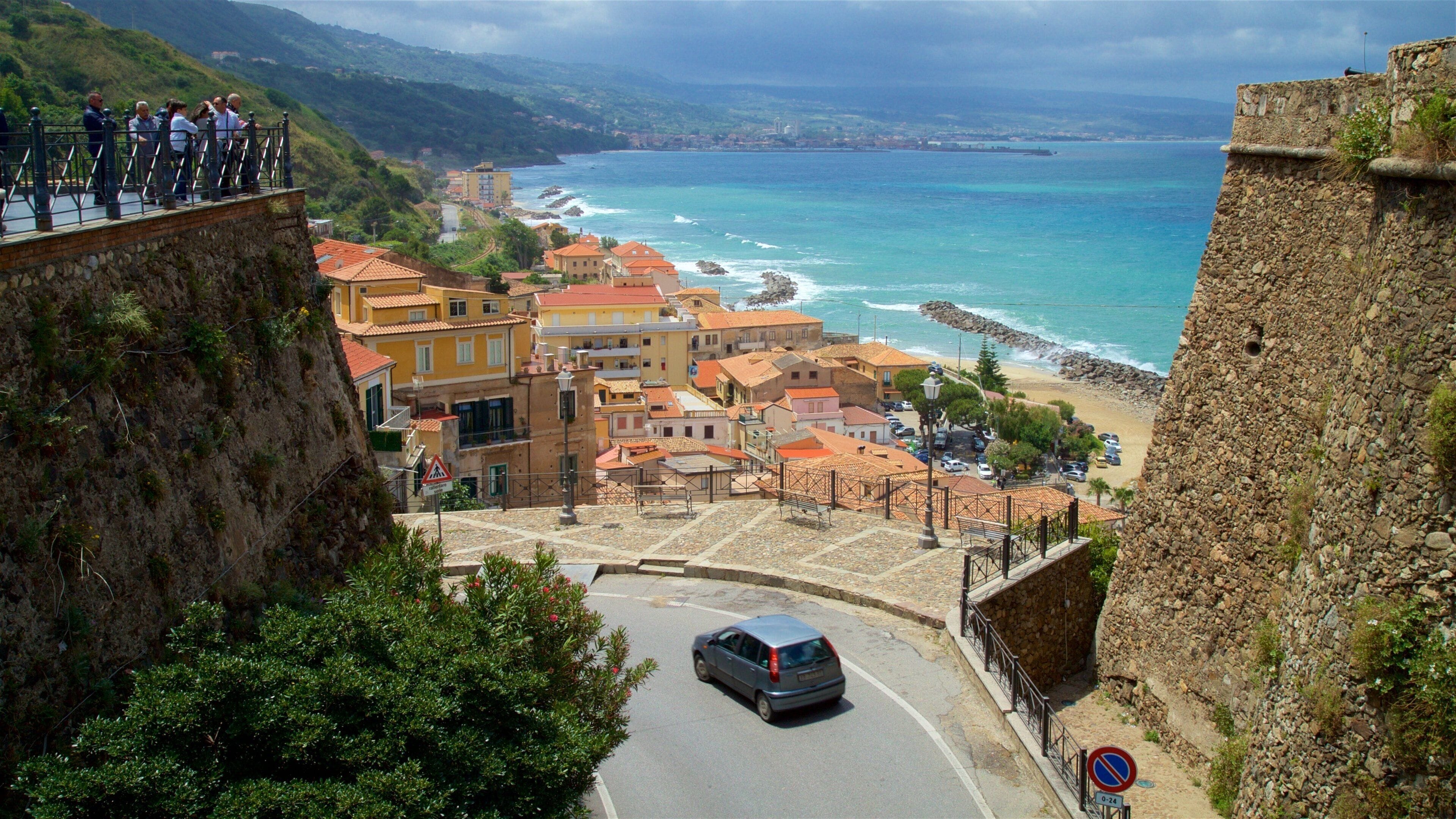 A coastal town with a stone fort, a winding road, and a view of the sea.