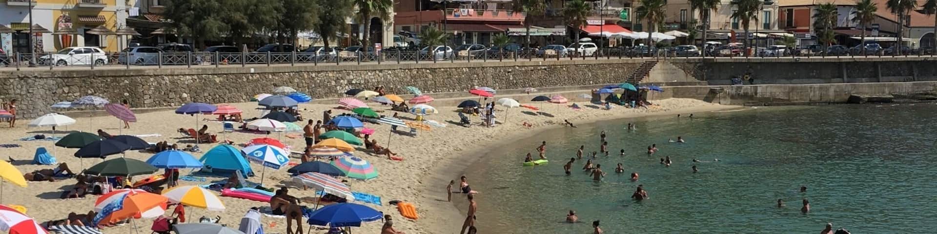 A crowded beach with people swimming and sunbathing, surrounded by colorful umbrellas and beach chairs.
