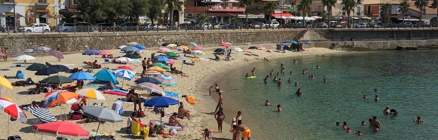 Una playa concurrida, gente nadando y tomando el sol, rodeada de sombrillas y sillas de playa coloridas.