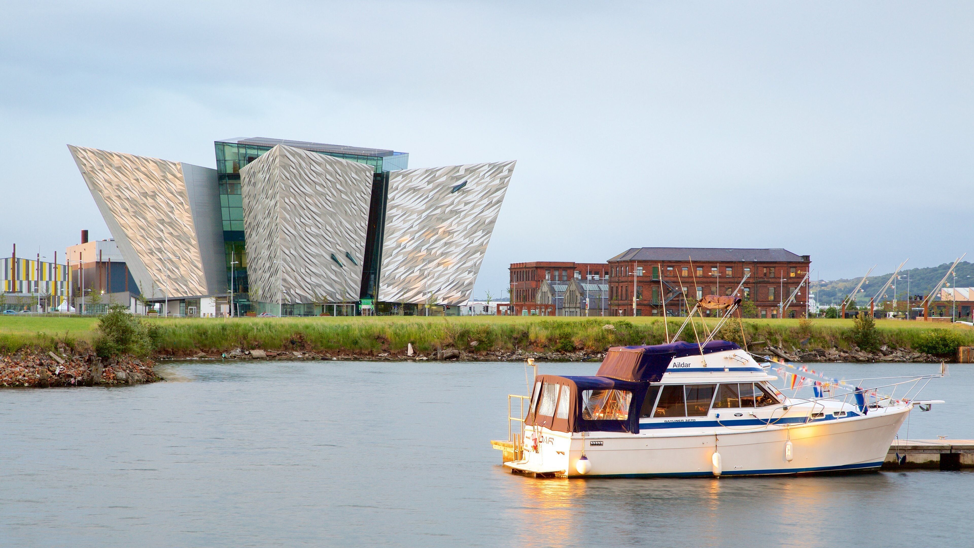 A modern building with a unique geometric facade, a river, and a boat docked near the shore.